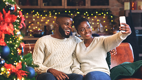 Happy couple celebrating Christmas fairy light social distancing festive red green Christmas tree knitted sweaters